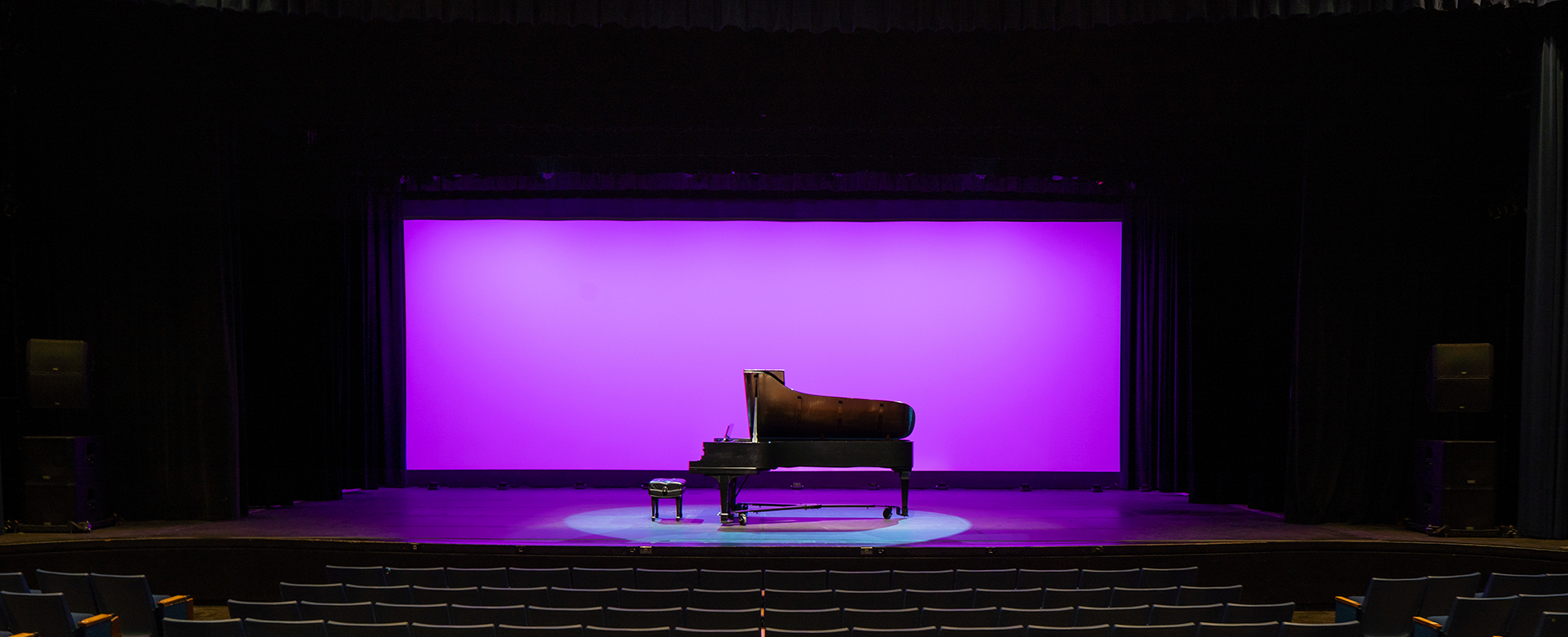 front-facing photo of a piano on a stage in front of a lavender colored drop curtain